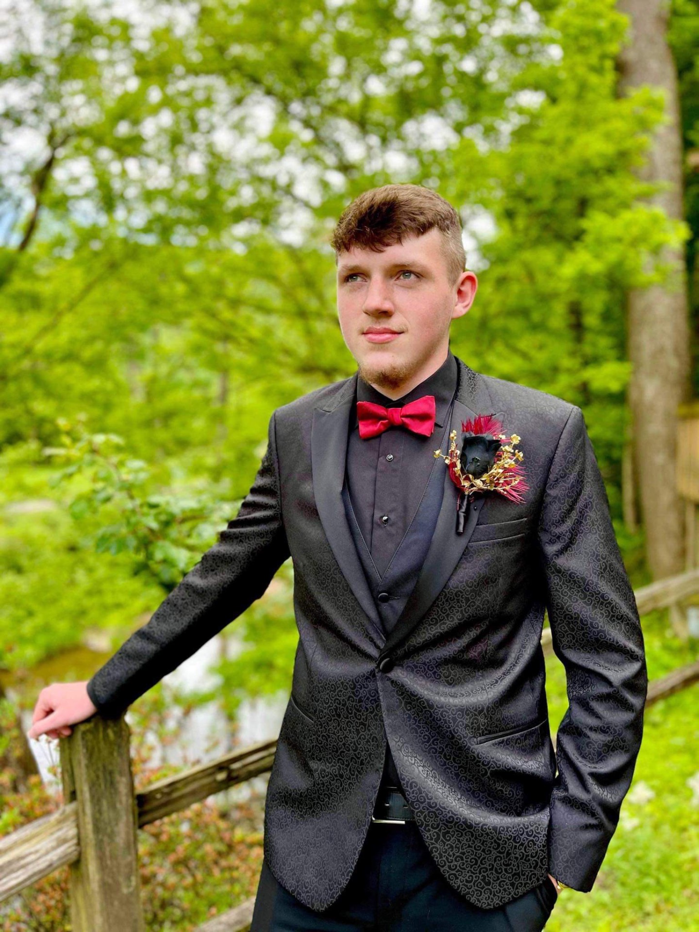 Young man in black paisley tuxedo with red bow tie and boutonnière